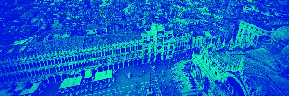 Monochrome photograph: an aerial view of St Mark’s Square in Venice with a blue and emerald green duotone effect. The bird’s-eye view shows St Mark’s Basilica in the bottom right, the Procuratie Nuove on the left and the Clock Tower in the centre. The square is filled with small human figures, whilst in the background the dense urban fabric of the city stretches out towards the lagoon, beneath a partly cloudy sky.