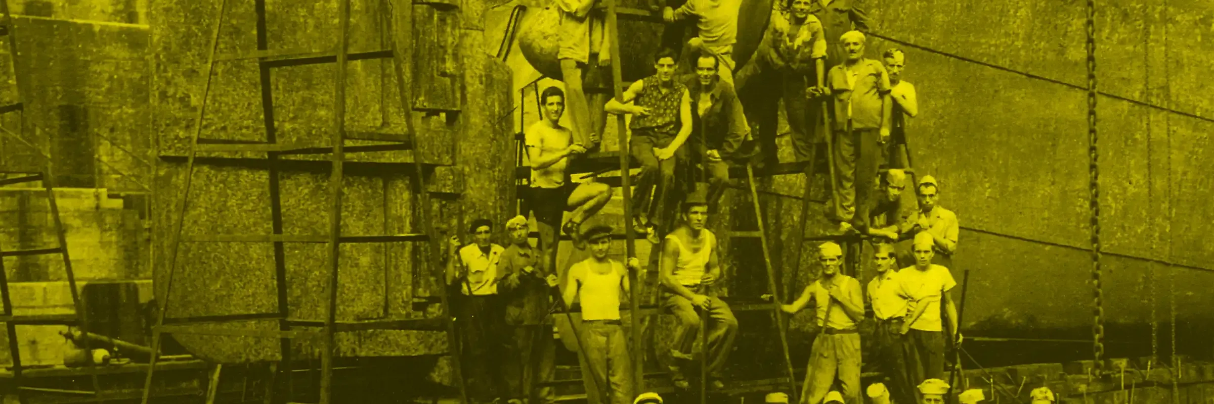 Gli ultimi arsenalotti - Immagine tematica: un gruppo di uomini, uno sopra l'altro a formare una piramide, al fianco di una chiglia navale. La foto è con dominante di colore giallo.